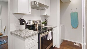 Una cocina moderna con armarios blancos, una campana extractora de acero inoxidable, una encimera de granito y un horno.