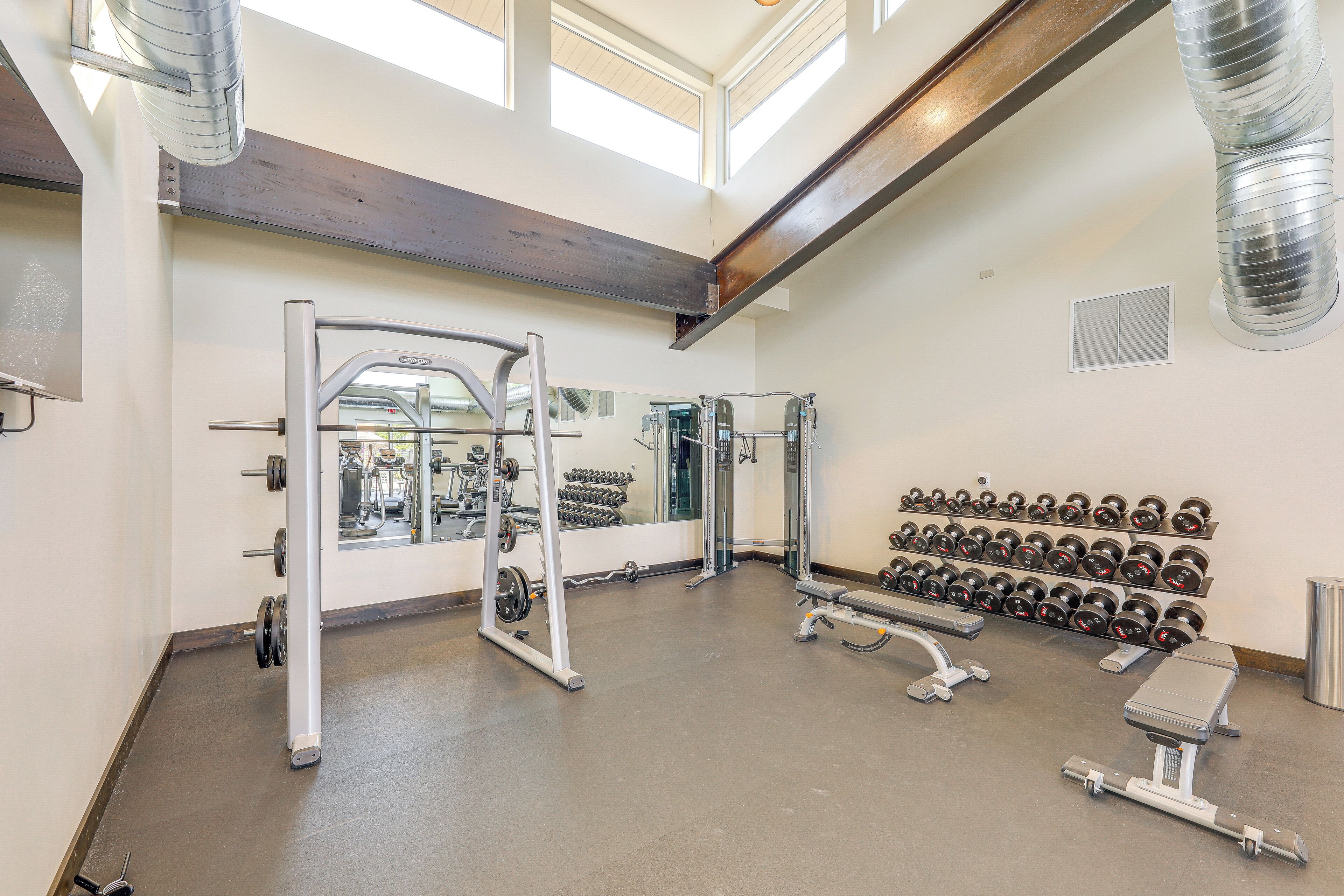 Un gimnasio con equipamiento para levantamiento de pesas, bancos y mancuernas.