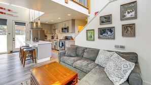 A spacious living area with a grey sofa, wooden coffee table, and a kitchen in the background. - 1 Mi to Lake: Upscale Condo in Whitefish Resort (Whitefish)