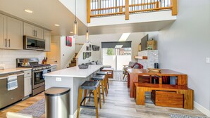 A modern kitchen with a central island, stainless steel appliances, and a wooden dining area. - 1 Mi to Lake: Upscale Condo in Whitefish Resort (Whitefish)