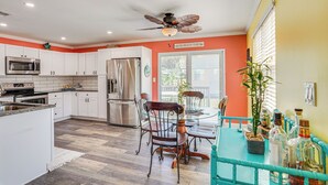 A kitchen with white cabinets, stainless steel appliances, and a dining area with a glass table and chairs. - Panama City Home w/ Fire Pit - Walk to Beaches! (Panama City Beach)