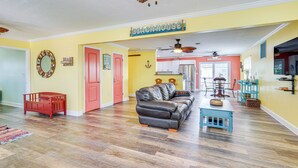 A spacious living room with a large sofa, a coffee table, and a dining area with chairs. There is a kitchen in the background, a ceiling fan, and a sign that reads "Beachhouse". - Panama City Home w/ Fire Pit - Walk to Beaches! (Panama City Beach)