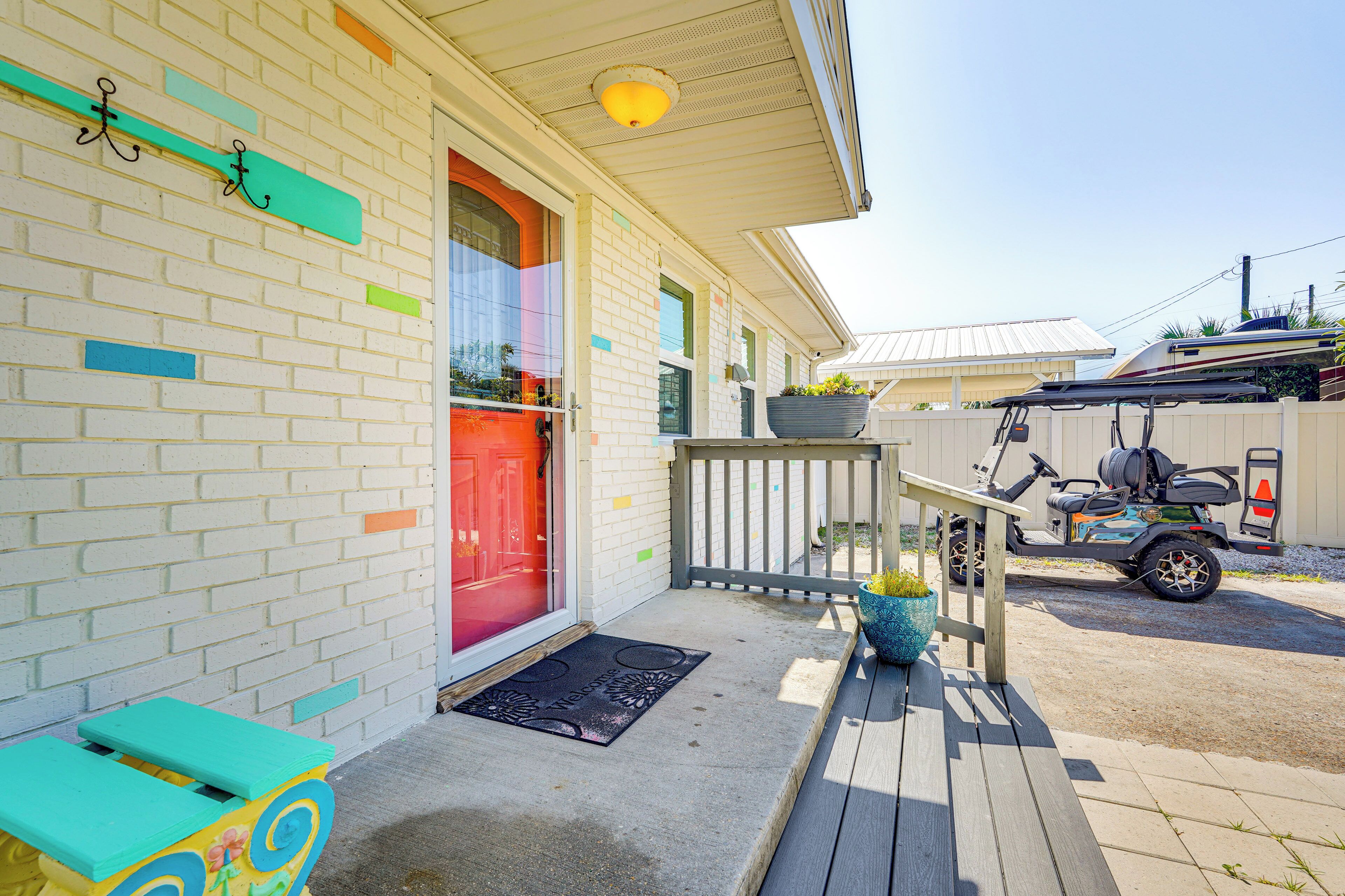 A house with a red door, a porch with a bench, and a golf cart parked outside.