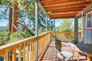 A wooden deck with a railing, a table, and two chairs, surrounded by trees.