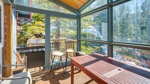 A covered outdoor area with a wooden table and chairs, a barbecue grill, and large windows offering a forest view. - Scenic Home w/ Sauna - 7 Mi to Heavenly Mountain! (Stateline)