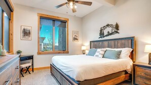 Une chambre à coucher avec un lit en bois, un bureau, une chaise, une commode et un ventilateur de plafond.