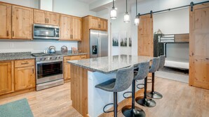 Une cuisine moderne dotée de meubles en bois, d’appareils électroménagers en acier inoxydable, d’un plan de travail en granit et d’un coin bar avec des tabourets.