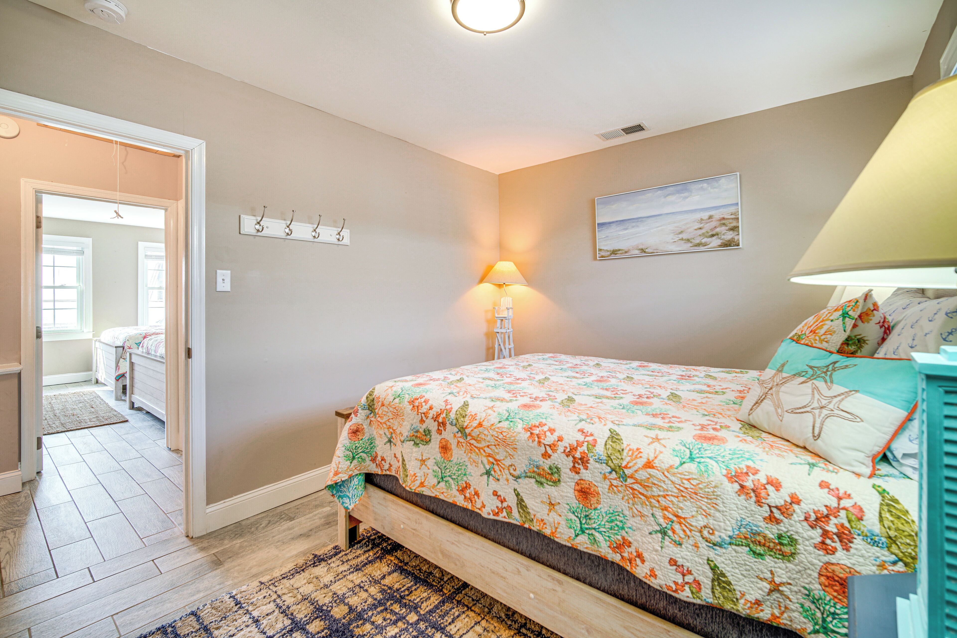 A bedroom with a bed, a nightstand, a lamp, a painting, and a door leading to another room.