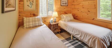 A cozy cabin room with two beds, wooden walls, a ceiling fan, and framed artwork.