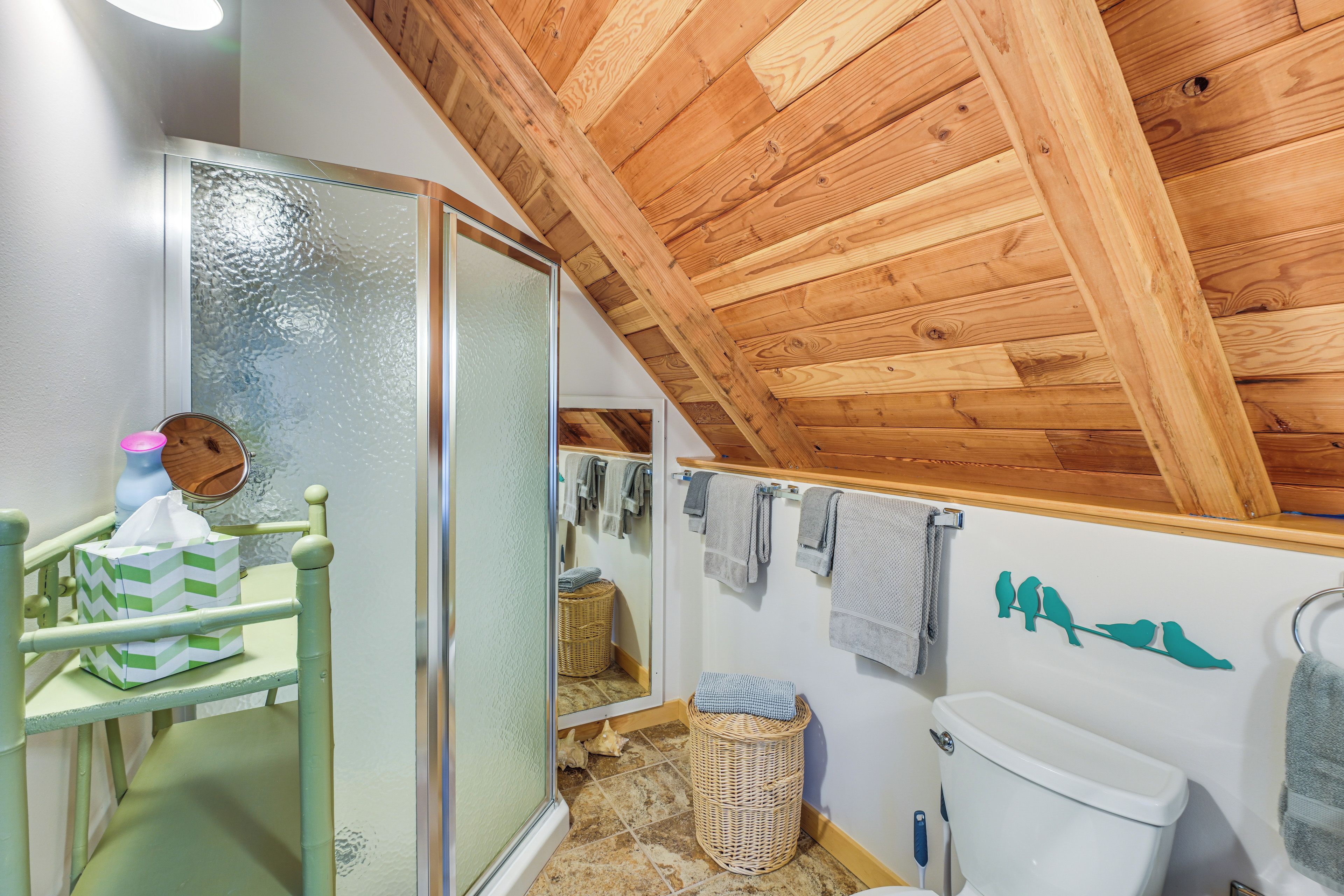 Ein Badezimmer mit Holzboden, einer Glasdusche, einer Toilette und einem Handtuchhalter mit Handtüchern.