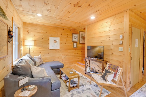 A cozy wooden cabin interior with a sofa, a TV, and a small table. - Cozy Acadia Area Cabin, Walking Distance to Ocean (Prospect Harbor)