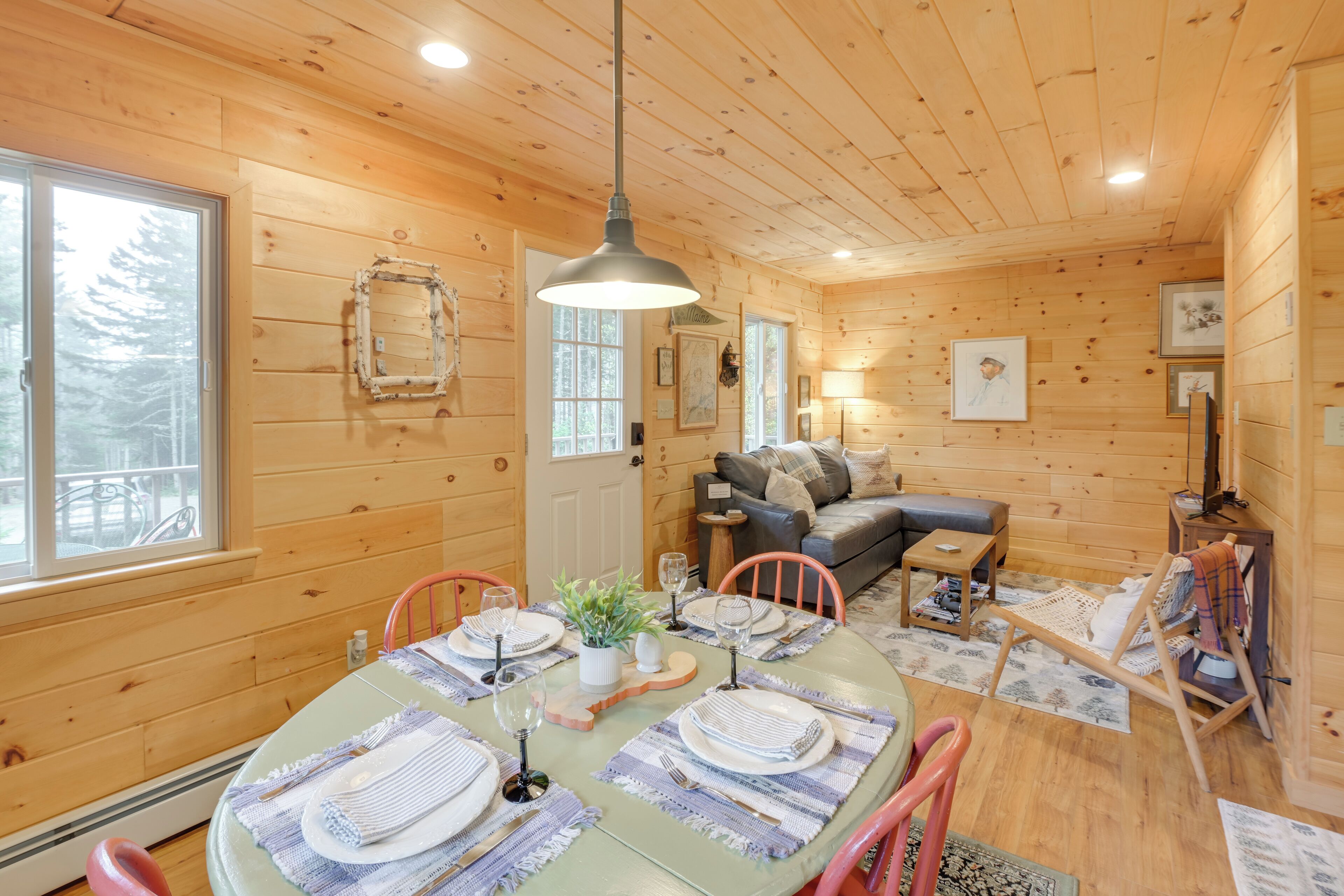 A cozy cabin interior with a dining area set for four, a sofa, and a small table with a lamp.