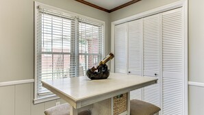 Una habitación de esquina con una mesa de color claro y dos sillas, un jarrón decorativo y un armario blanco con puertas persianas.
