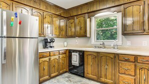 Una cocina con armarios de madera, refrigerador de acero inoxidable, lavavajillas y ventana con vista a follaje.