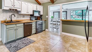 A kitchen with white cabinets, a stainless steel oven, and a dishwasher. There is a window with a view of a patio. - Spacious Micanopy Farmhouse w/ Luxurious Pool! (Micanopy)