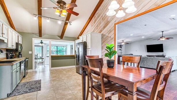 A spacious kitchen with wooden beams, a dining area with a wooden table and chairs, and a large window. - Spacious Micanopy Farmhouse w/ Luxurious Pool! (Micanopy)