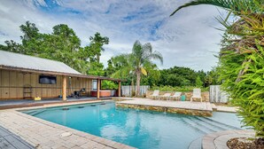 A swimming pool with a wooden deck, lounge chairs, and a building with a metal roof in the background. - Spacious Micanopy Farmhouse w/ Luxurious Pool! (Micanopy)