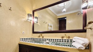 A bathroom with a large mirror, dark wooden cabinets, a tiled countertop, and a patterned floor. - Riad (Marrakech)