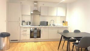 A modern kitchen with white cabinets, a built-in oven, a sink, and a dining area with a table and chairs. - Cosy Modern Townhouse, 5mins to Tube, 02, Excel (London)