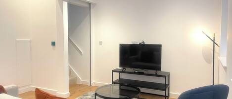 A modern living room with a flat-screen TV on a glass stand, a blue chair, and a white sofa.