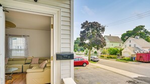 Ein Wohnzimmer mit einem beigen Sofa, einem Glastisch und Blick auf eine Straße mit Häusern und einem Baum.