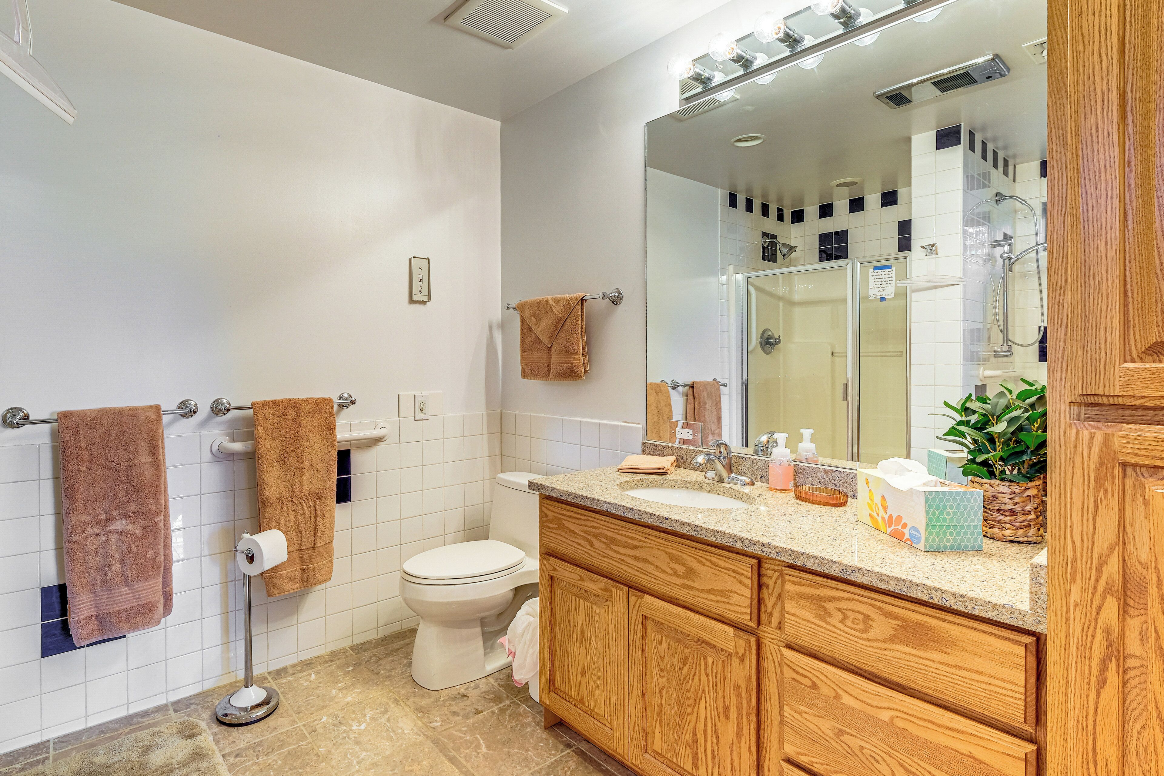 A bathroom with a white toilet, a wooden vanity with a sink, and a large mirror.