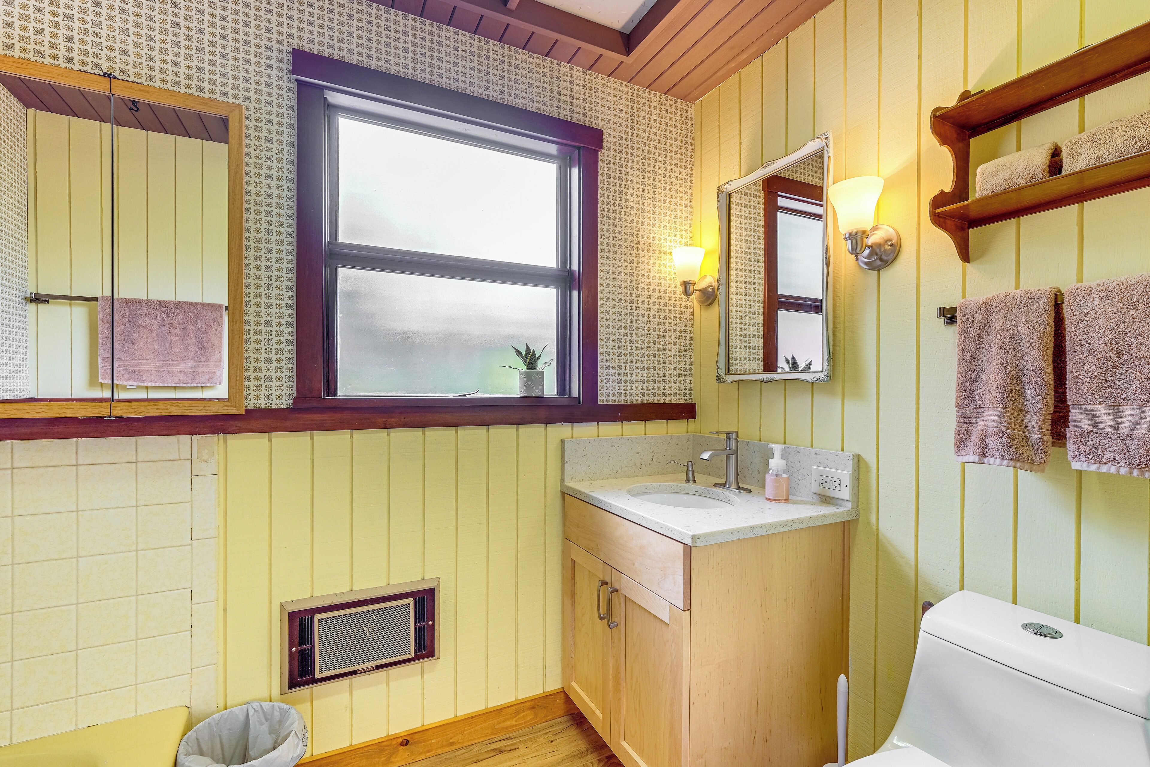 A bathroom with a wooden vanity, a window, a mirror, and a towel rack.