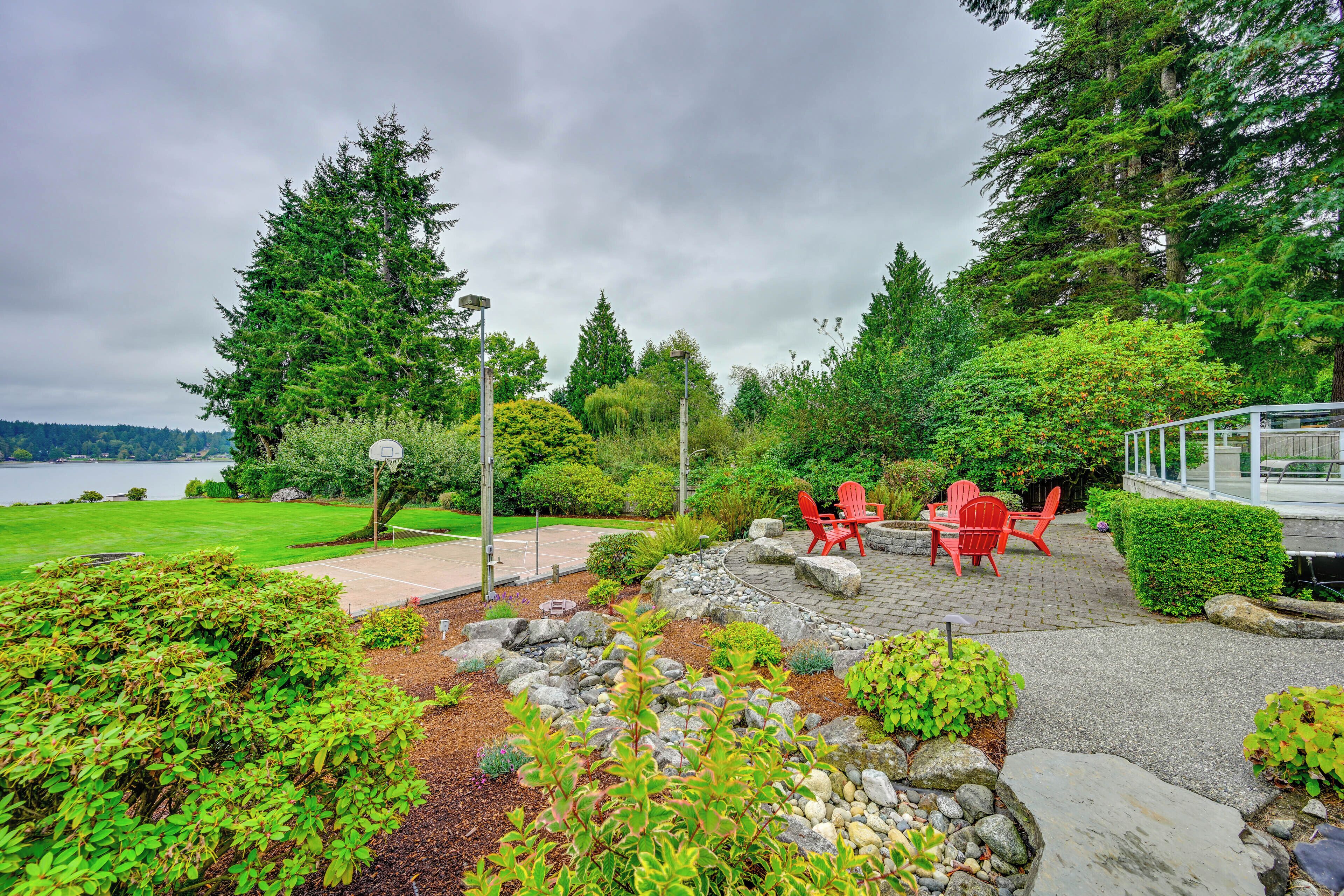 A landscaped garden with a patio area featuring red chairs and a table, surrounded by various plants and trees.