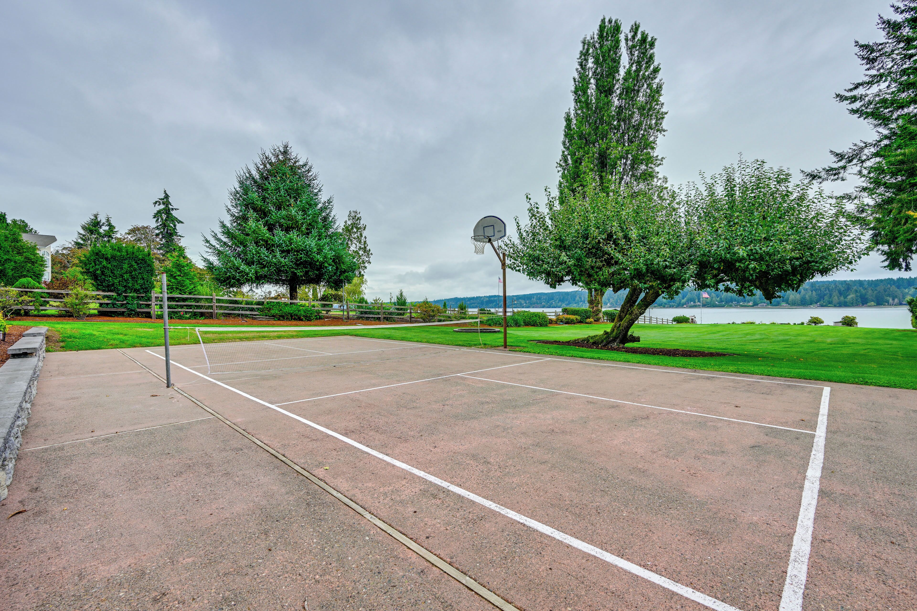 Una cancha de baloncesto al aire libre con aro, rodeada de árboles y vista a un lago.