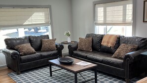 A living room with two black leather sofas, a wooden coffee table, and a patterned rug. -  Quaint,newly remodeled country cabin in the heart of Bourbon Country. (Raywick)