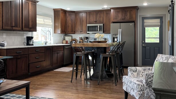 A modern kitchen with wooden cabinets, a central island with bar stools, a refrigerator, and a microwave. -  Quaint,newly remodeled country cabin in the heart of Bourbon Country. (Raywick)