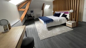 Ein modernes Schlafzimmer mit schrägem Dach, einem Bett mit Holz-Kopfteil, einem Schreibtisch mit Stuhl und einem kleinen Tisch mit Lampe.