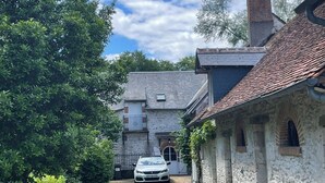 Ein Steinhaus mit einem geparkten Auto davor, umgeben von viel Grün und blauem Himmel.