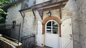 Ein Steinhaus mit einer weißen Tür, einem Balkon und einem schwarzen Metallzaun.