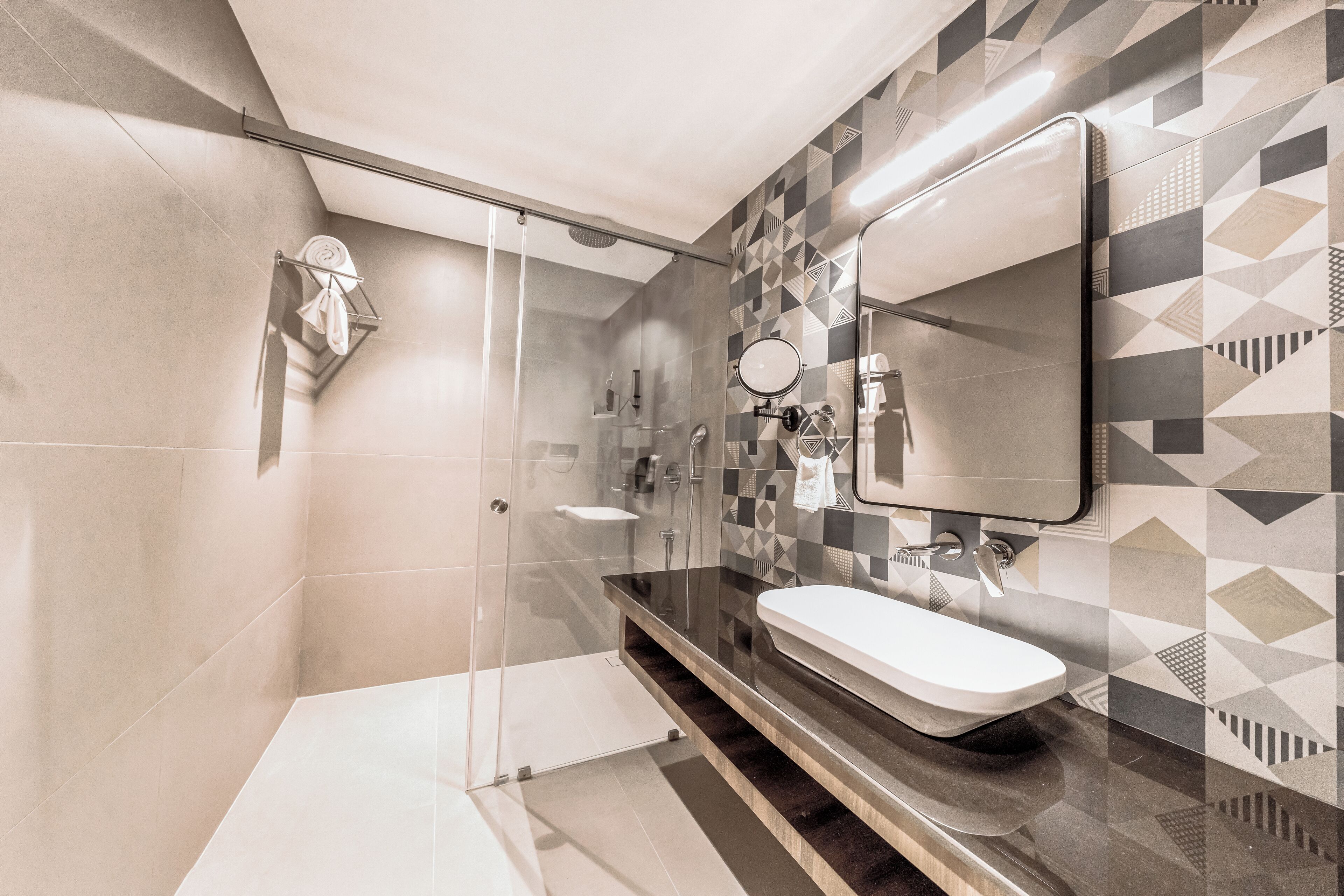 Une salle de bain moderne avec une douche à parois de verre, un meuble-lavabo et un mur orné d’un motif géométrique.