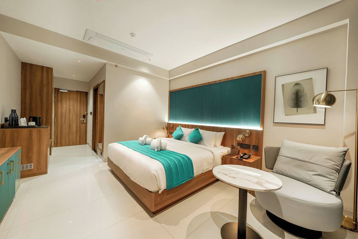 A modern hotel room with a large bed, a sitting area, a desk, and a bathroom.