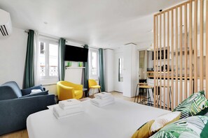 A modern hotel room with a large bed, a sofa, a yellow chair, and a desk with a computer.