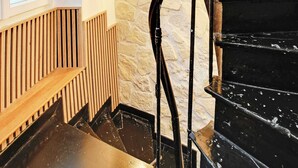 Eine Wendeltreppe mit schwarzer Handläufe und Holzstufen, die zu einer Empore mit einer Steinwand und einem Fenster führt.