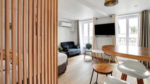 Ein modernes Hotelzimmer mit einer Holzwand, einer Couch, einem Esstisch mit Stühlen und einem an der Wand befestigten Fernseher.