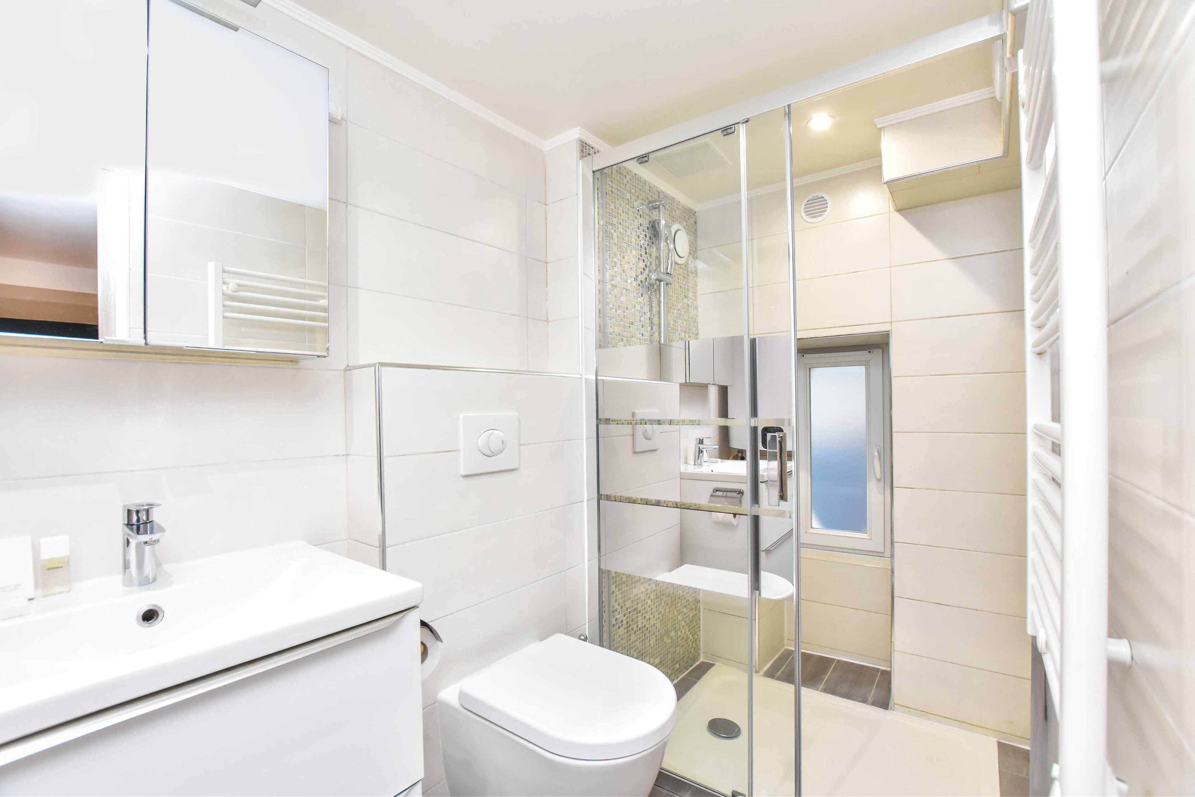 A modern bathroom with a white sink, toilet, and glass-enclosed shower area.