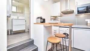 Eine kleine Küche mit Mikrowelle, Backofen und Kaffeemaschine. Zwei Hocker und eine Waschmaschine sind vorhanden.