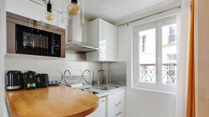 Eine kleine Küche mit einer Mikrowelle, einem Wasserkocher und einem Toaster auf der Arbeitsfläche, einem Spülbecken und einem Fenster mit Balkonblick.
