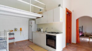 A compact kitchen with a gas stove, oven, and white cabinets. There is a small dining area with a chair and a table. - 4024 Casina Litta by Barbarhouse (Cutrofiano)