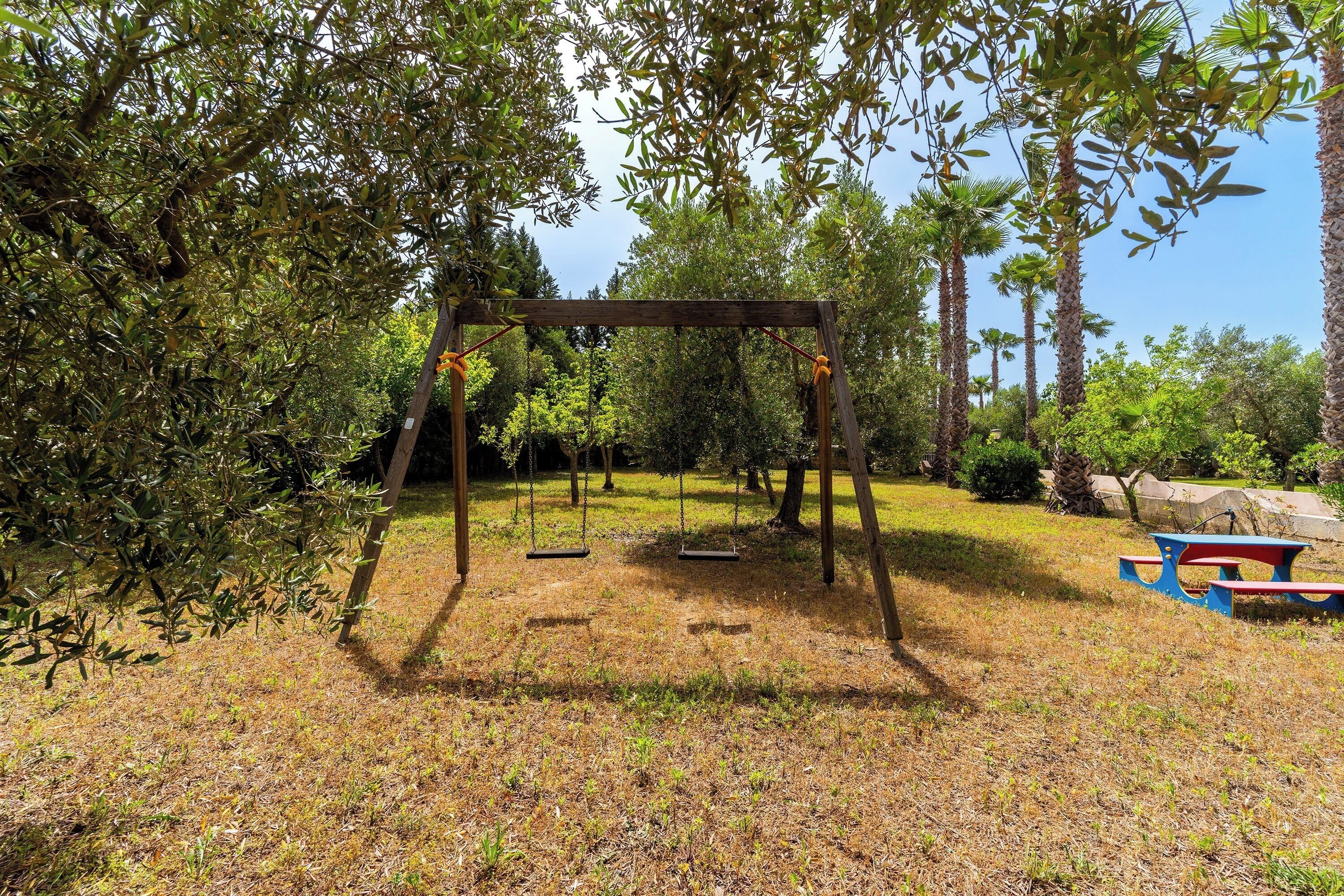 A wooden swing set in a park with a picnic table nearby.