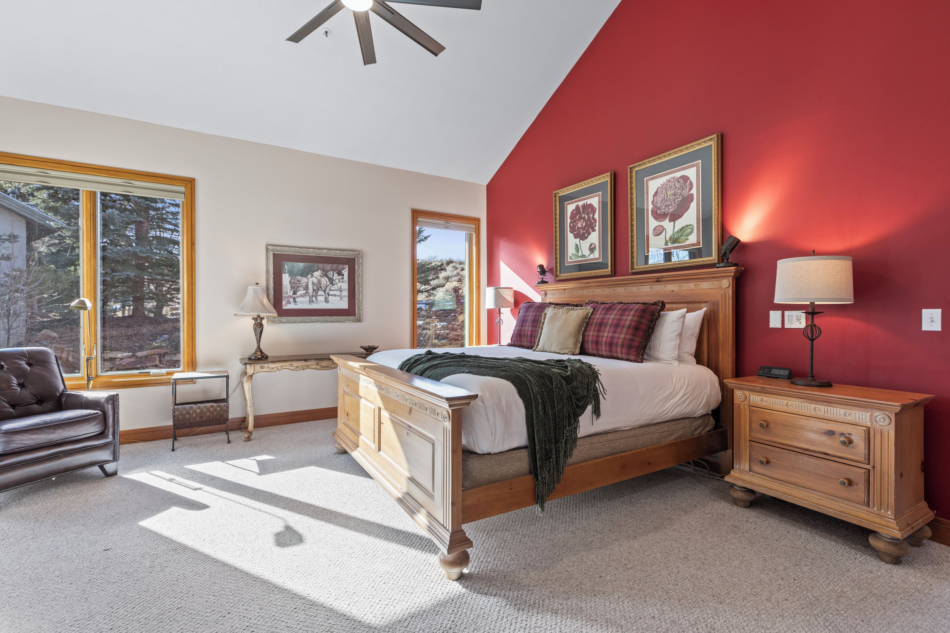 A bedroom with a large bed, a nightstand, a dresser, and two windows.