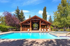 A pool area with a wooden pavilion, lounge chairs, and a clear blue pool.