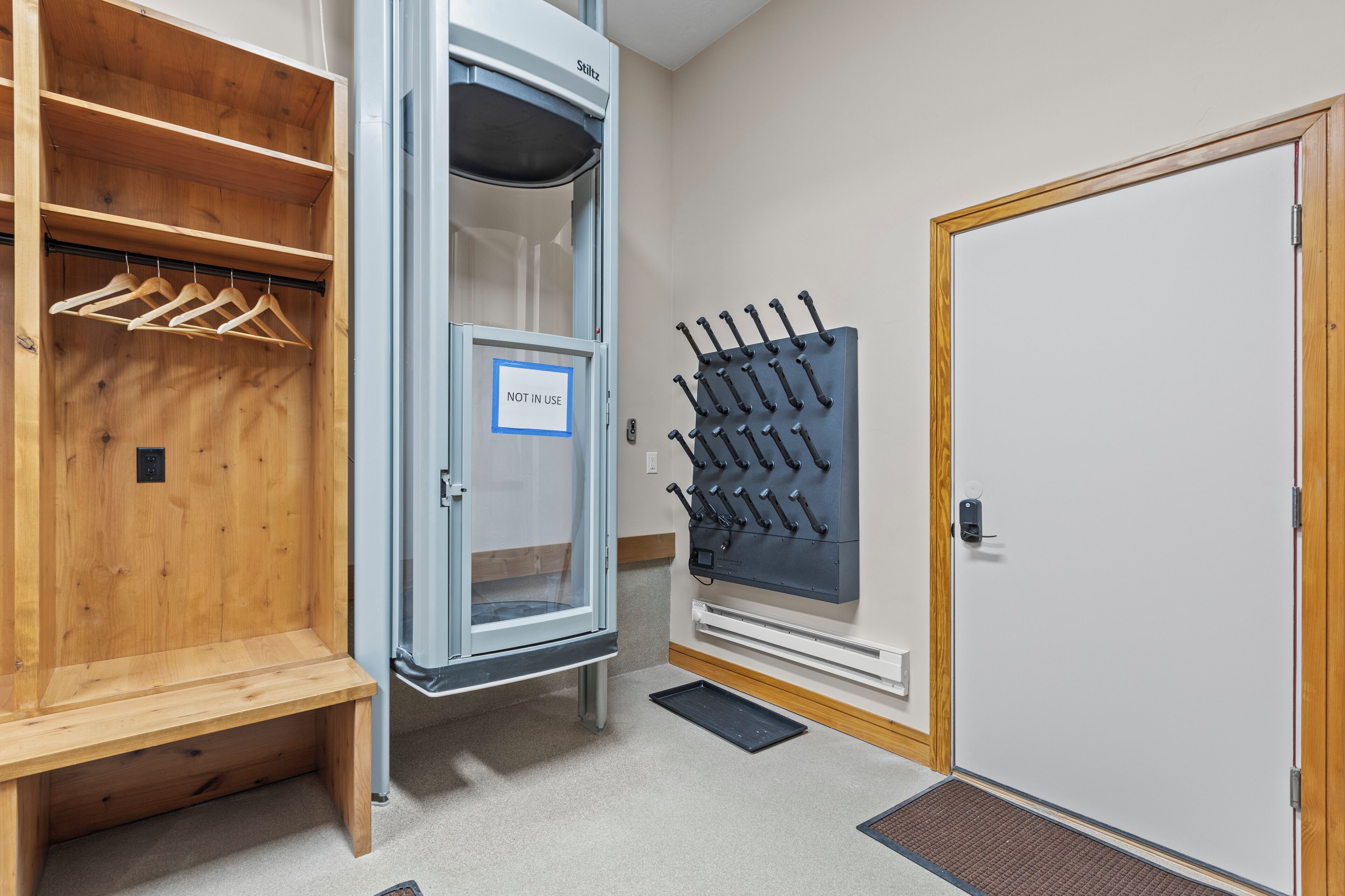A room with a wooden bench, a storage unit with a 'NOT IN USE' sign, a coat rack, and a door with a handle.