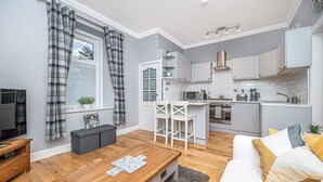 A modern living room with a wooden coffee table, a sofa with cushions, a TV, and a window with curtains. - The Wee Haig - 1 Bedroom Condo (Glenrothes)