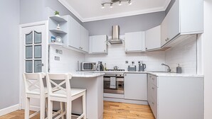 A modern kitchen with white cabinetry, a built-in microwave, and a stove. - The Wee Haig - 1 Bedroom Condo (Glenrothes)
