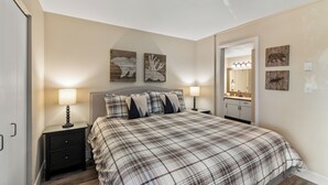 Een slaapkamer met een geruit sprei, twee kunstwerken aan de muur, een bedlamp en een nachtkastje.